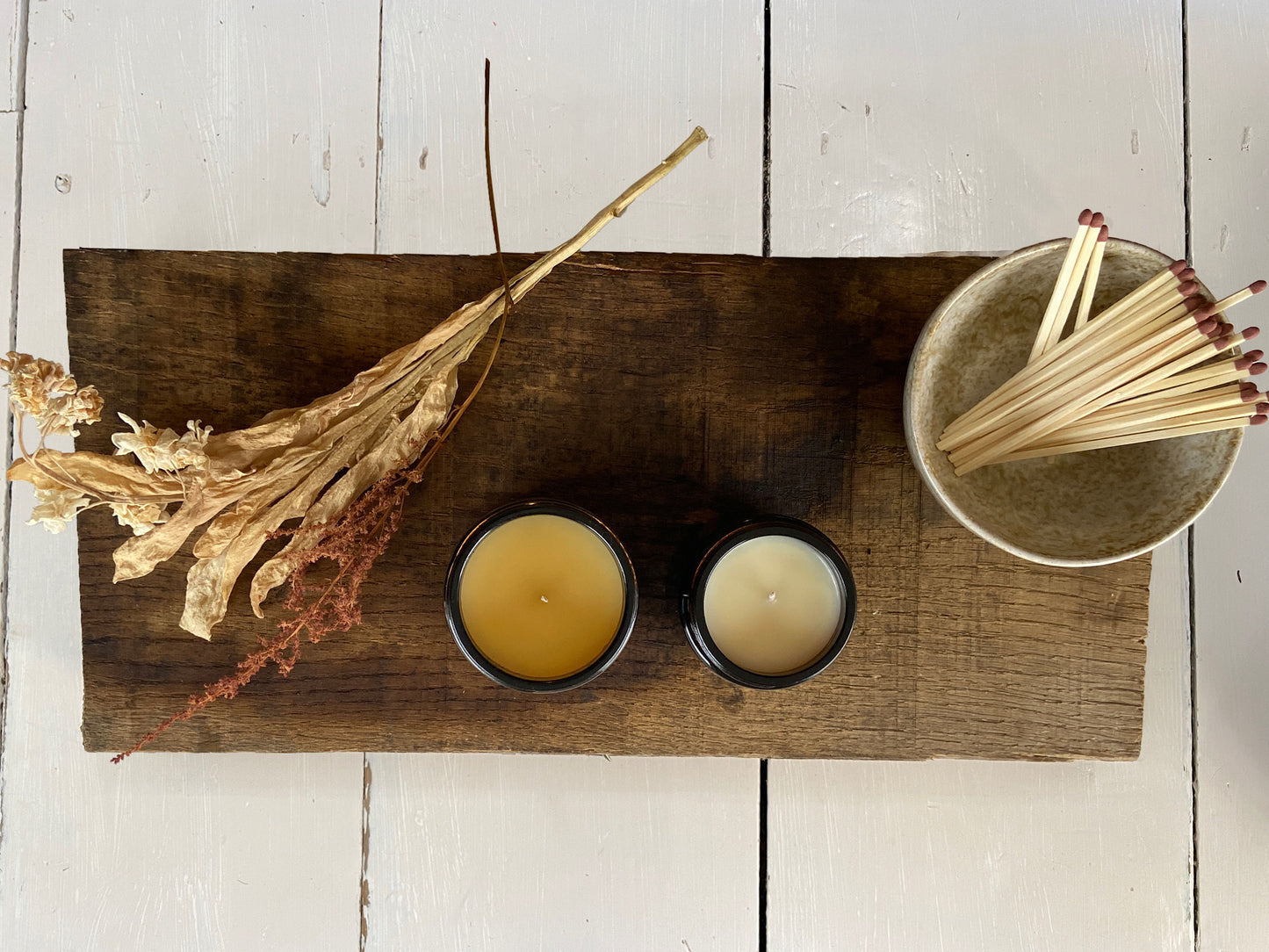 Plant wax and essential oil candles in relaxing natural blends. Both candles are in amber glass jars along side extra long matches and dried flowers.