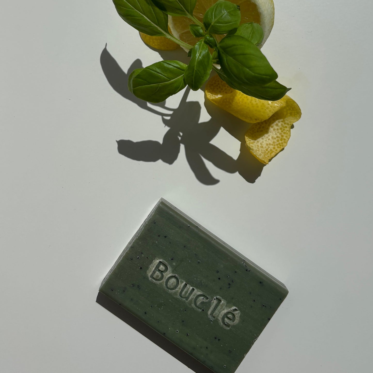 Green bar of soap labeled 'Boucle' on a white surface with lemon slices and leaves.