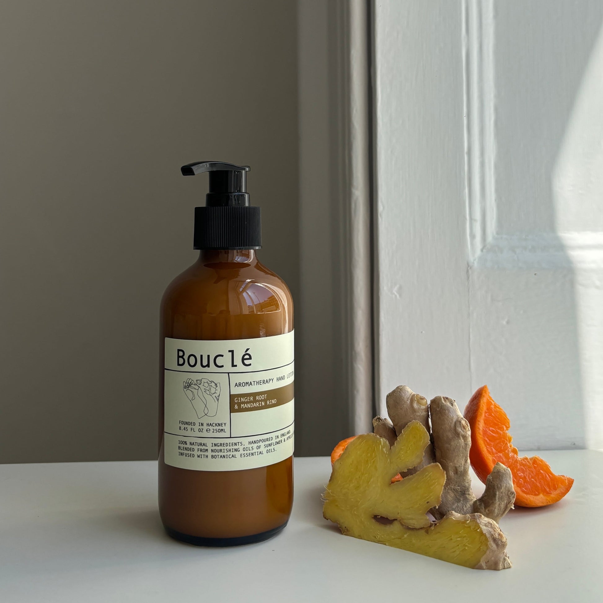Bottle of Bouclé all natural essential oil hand lotion next to botanical ingredients