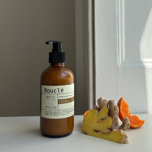 Bottle of Bouclé all natural essential oil hand lotion next to botanical ingredients