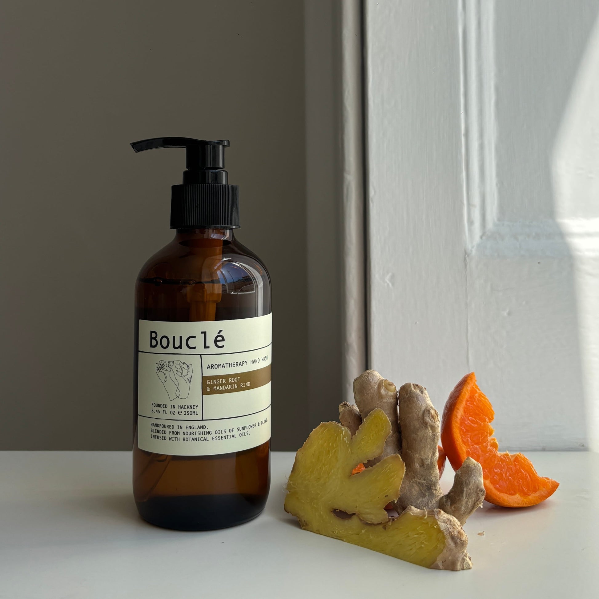 Bottle of Boucle  ginger and mandarin essential oil handwash surrounded by botanical ingredients. 