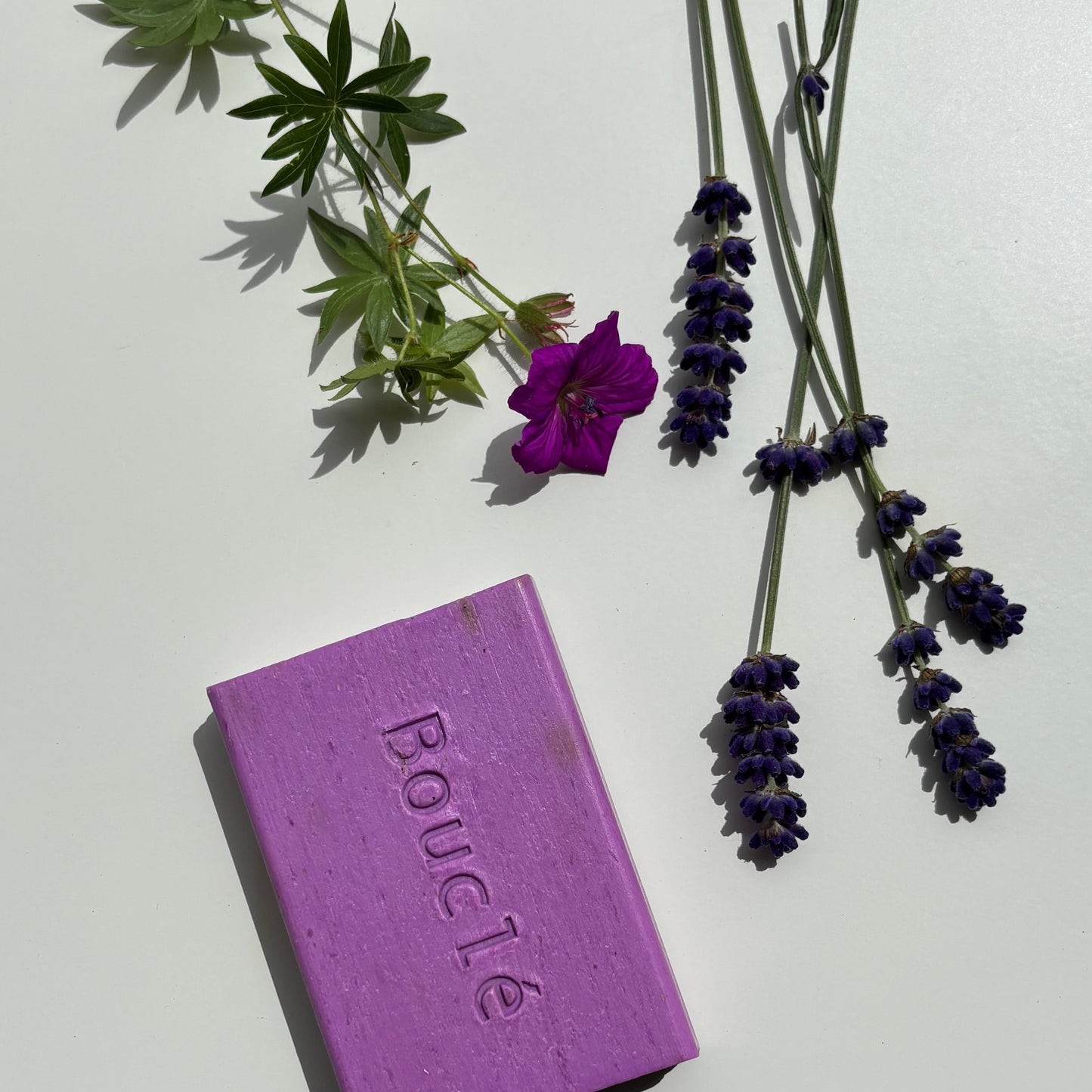 Purple soap bar with 'Boucle' branding and lavender flowers on a white surface