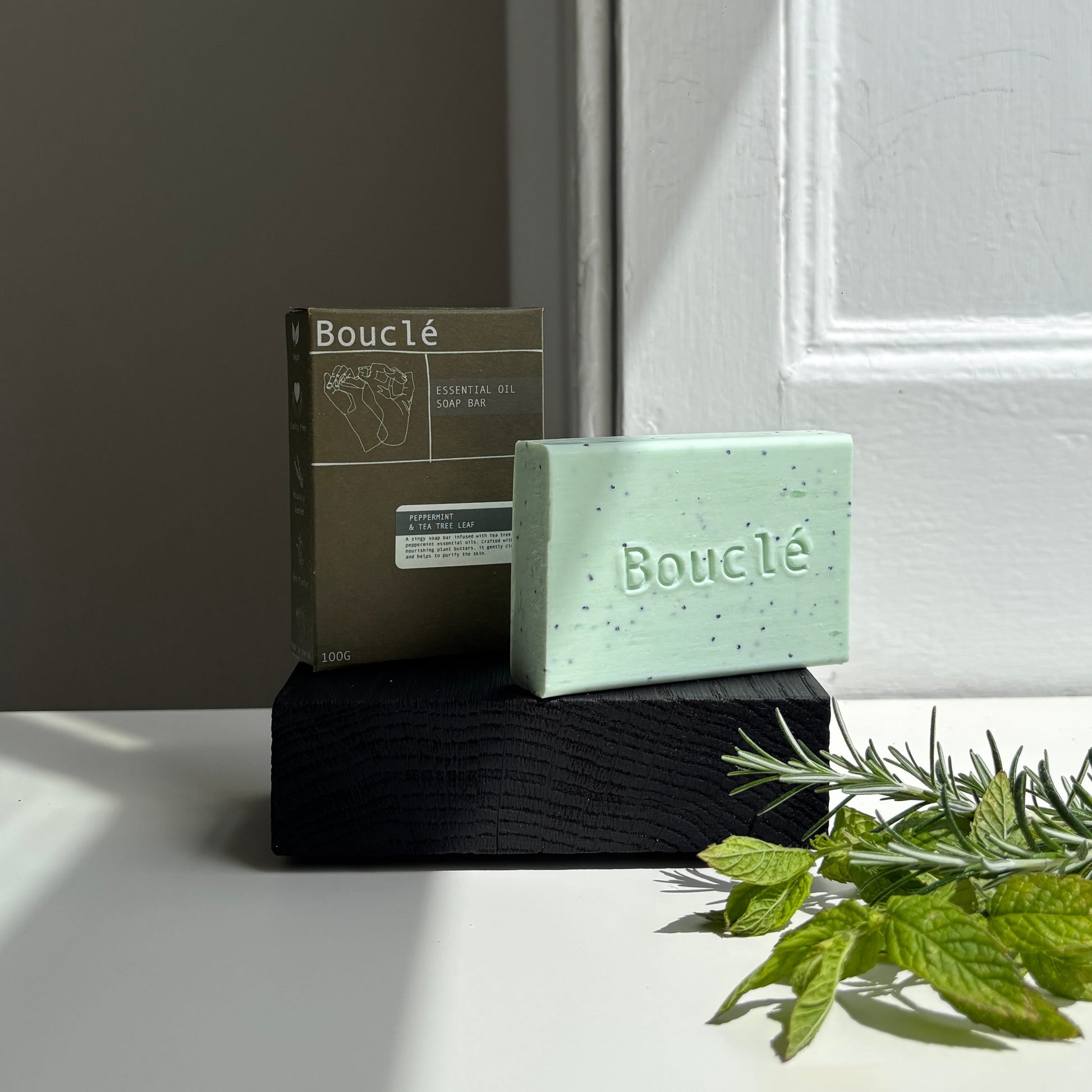 Green soap bar with packaging on a white surface, next to green leaves.