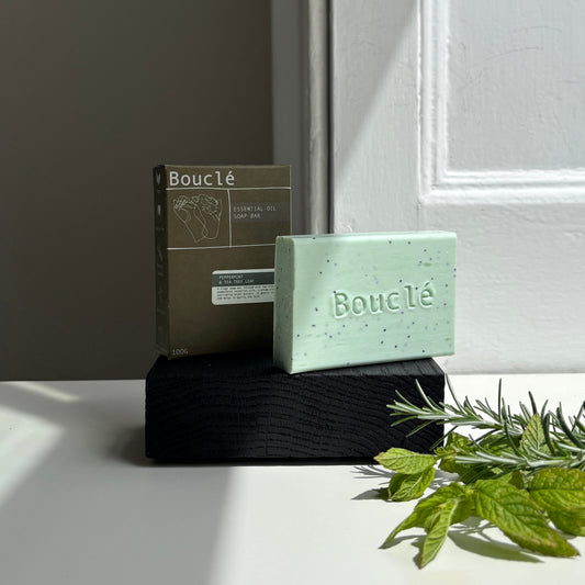 Green soap bar with packaging on a white surface, next to green leaves.