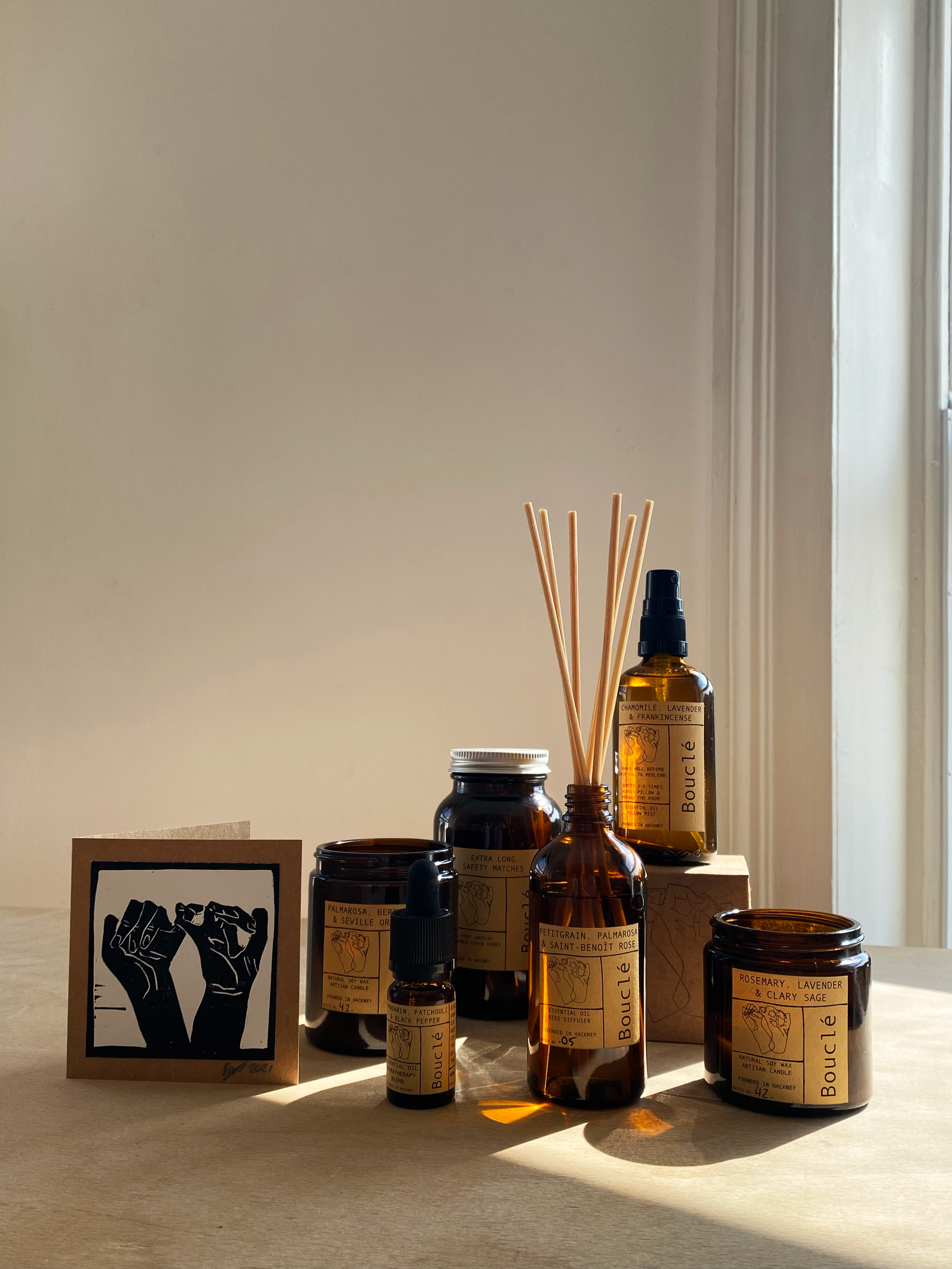 Selection of Bouclé London handpoured essential oil products in amber glass apothecary jars including soy wax candles, rattan reed diffusers, room sprays and essential oil aromatherapy blends.