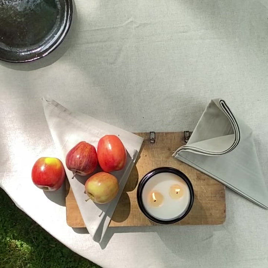 Video of a Bouclé large luxury Citrus, Rosemary & Lavender soy candle burning on a  minimal rustic table with some apples. Made in East London & Brighton.
