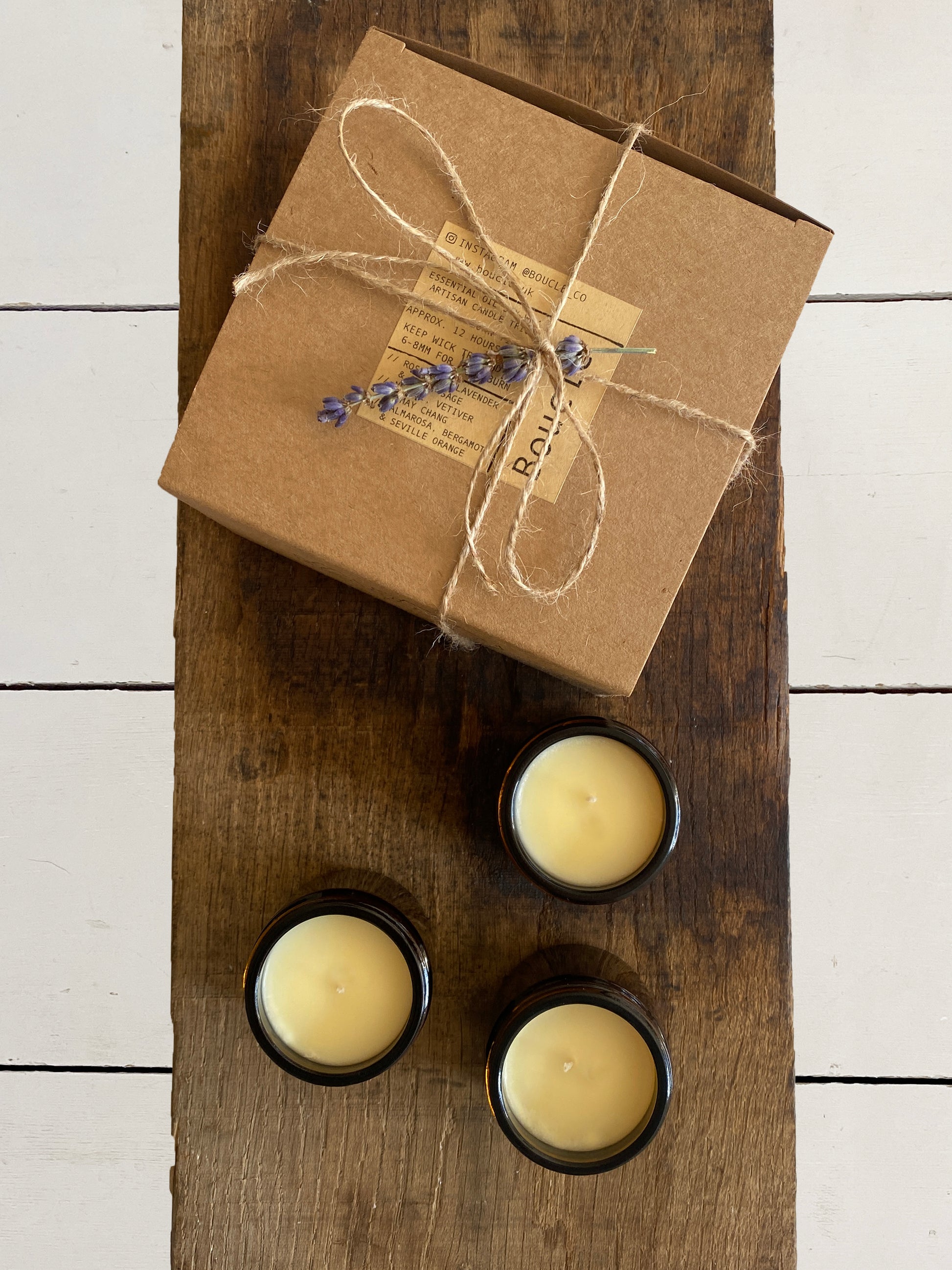 Gift wrapped mini candle gift set. Trio of candles beside recycled kraft gift box tied with ribbon and a sprig of dried lavender making the perfect local gift