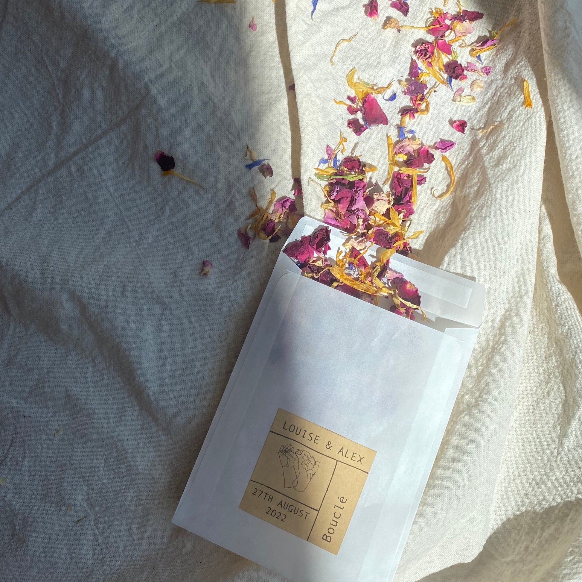 Dried real petal flower biodegradable natural wedding confetti pouch with a personalised label ideal for wedding styling. The petals are multicolour pink, yellow, purple and cream.