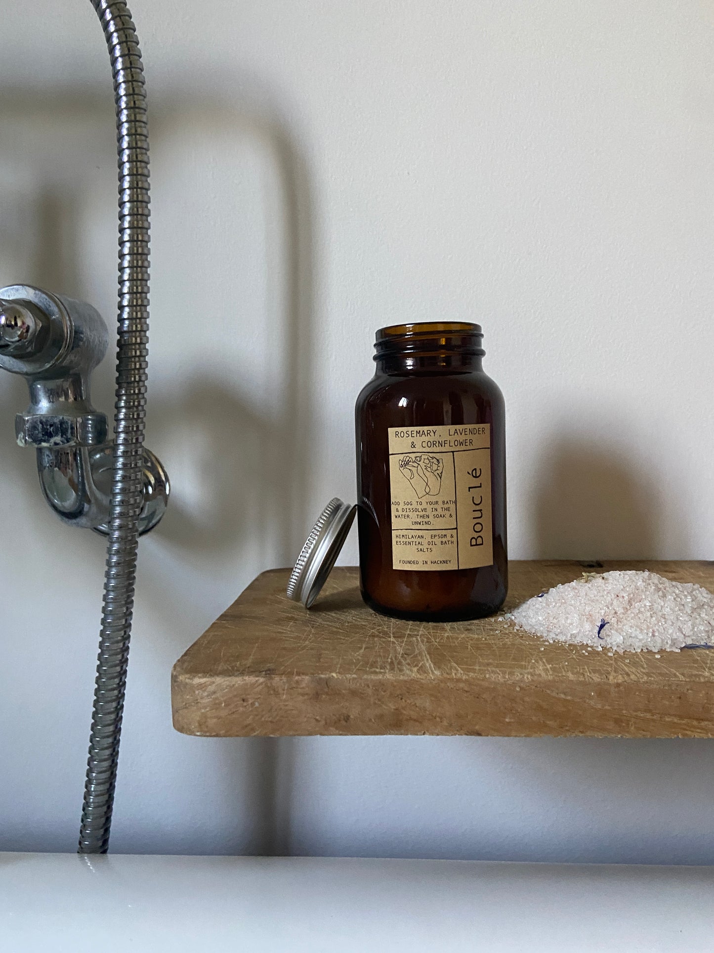 Rosemary, Lavender & Cornflower mineral rich bath salts on wooden board beside the bath. Made by Bouclé in East London & Brighton