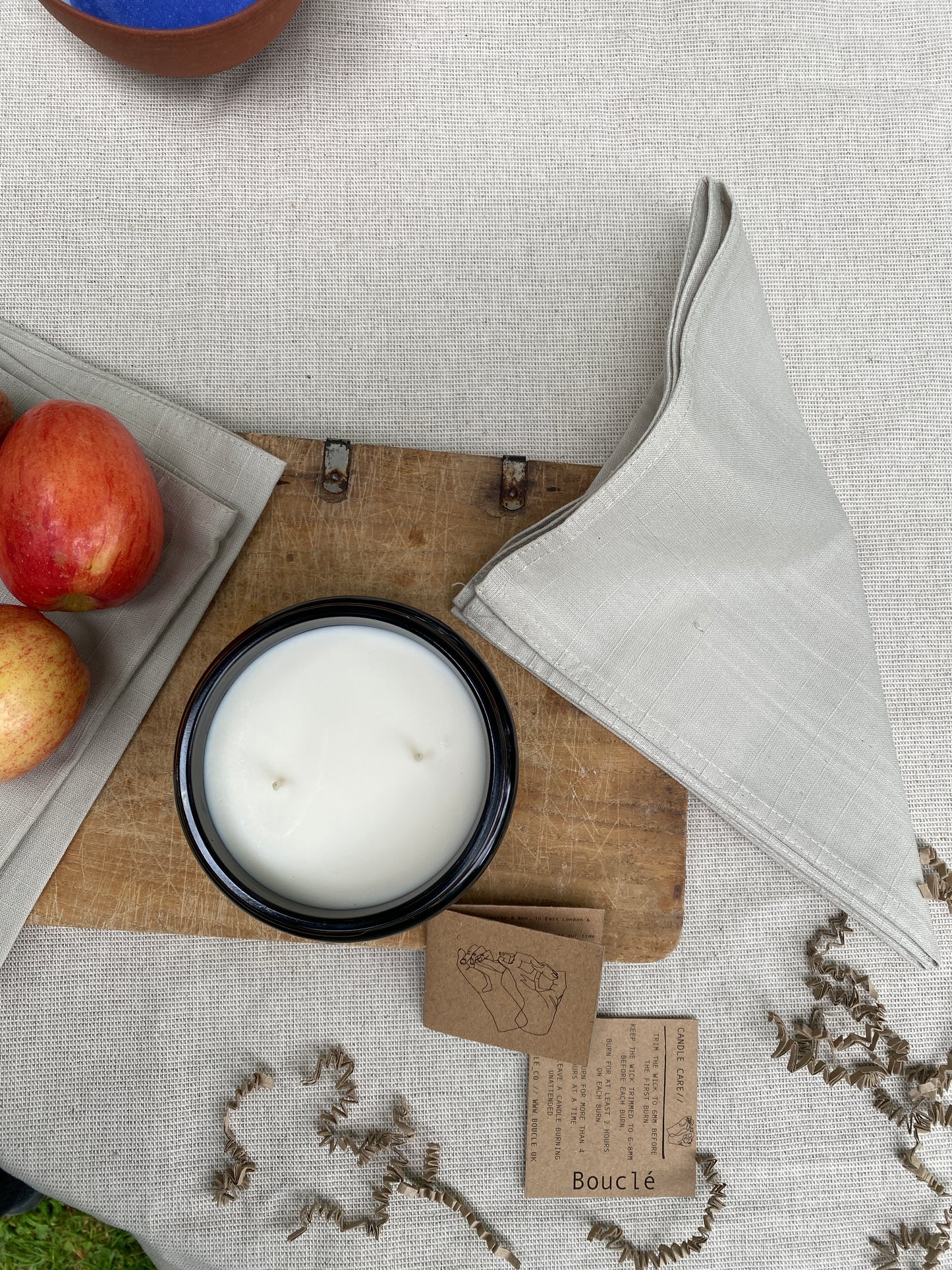 Bouclé Hackney soy wax candle made with essential oils on a minimal styled table surrounded by recycled krinkle gift packaging.