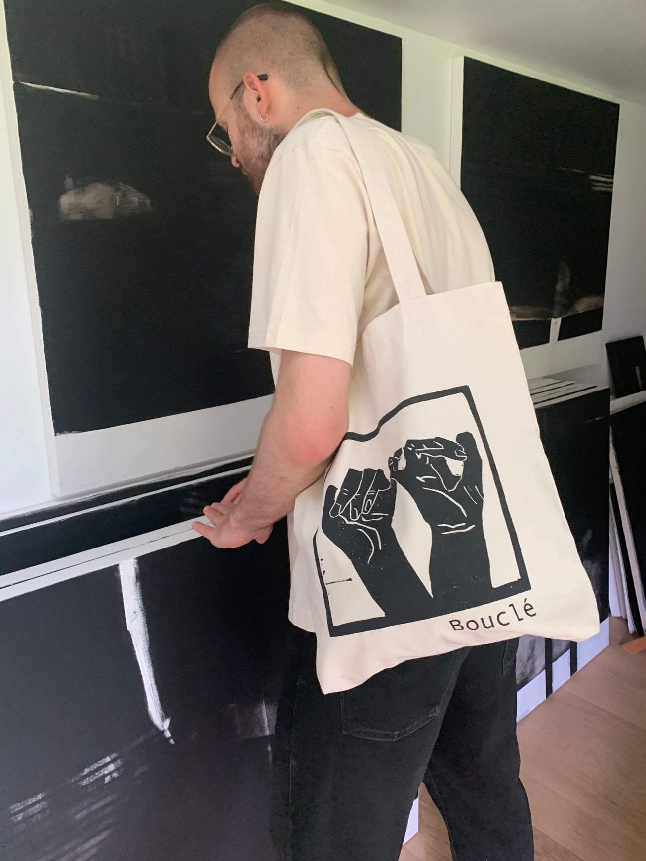 Ben wearing a Bouclé shopper bag with a print of the brand Interlinked Hands print on cream tote bag