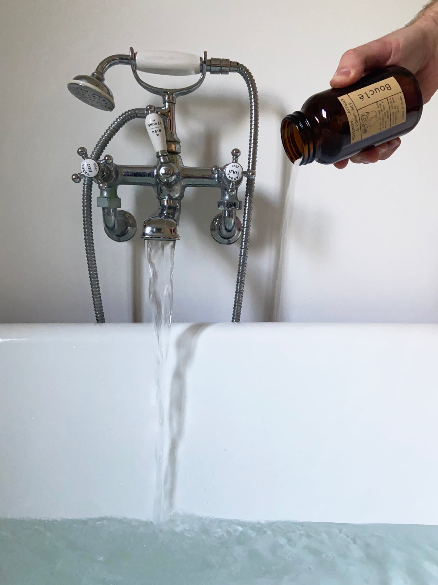 Epsom bath salts in apothecary style jar being poured into a bath for soothing